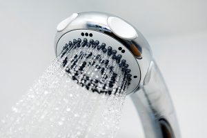 A showerhead sprays water droplets downward, with several small nozzles visible, against a plain white background.